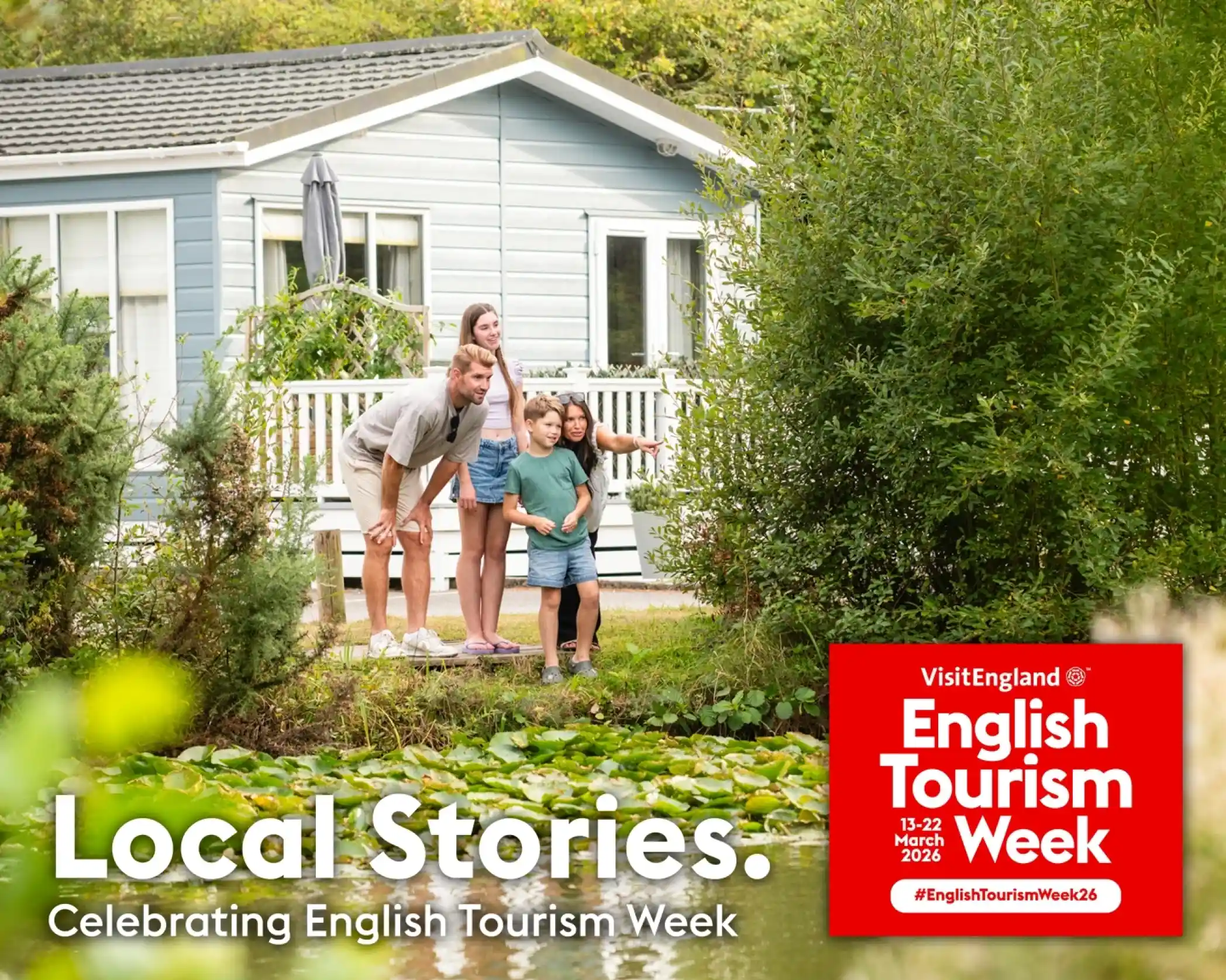 A family of four, including two children, stands by a serene pond near a light blue holiday home. They are engaged in a moment of curiosity, looking into the water surrounded by greenery. The text on the image promotes "English Tourism Week" with the dates of March 13-22, 2026, and emphasizes "Local Stories."