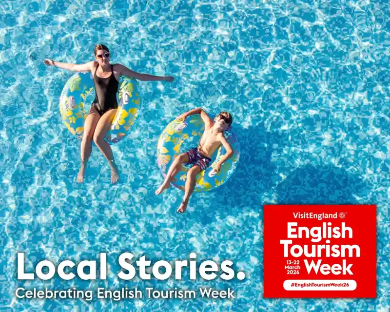 Two people float on colorful inner tubes in a clear blue swimming pool. The sun shines brightly overhead, and there’s a text overlay promoting English Tourism Week with the date March 13-22, 2026. The theme “Local Stories” is also highlighted.