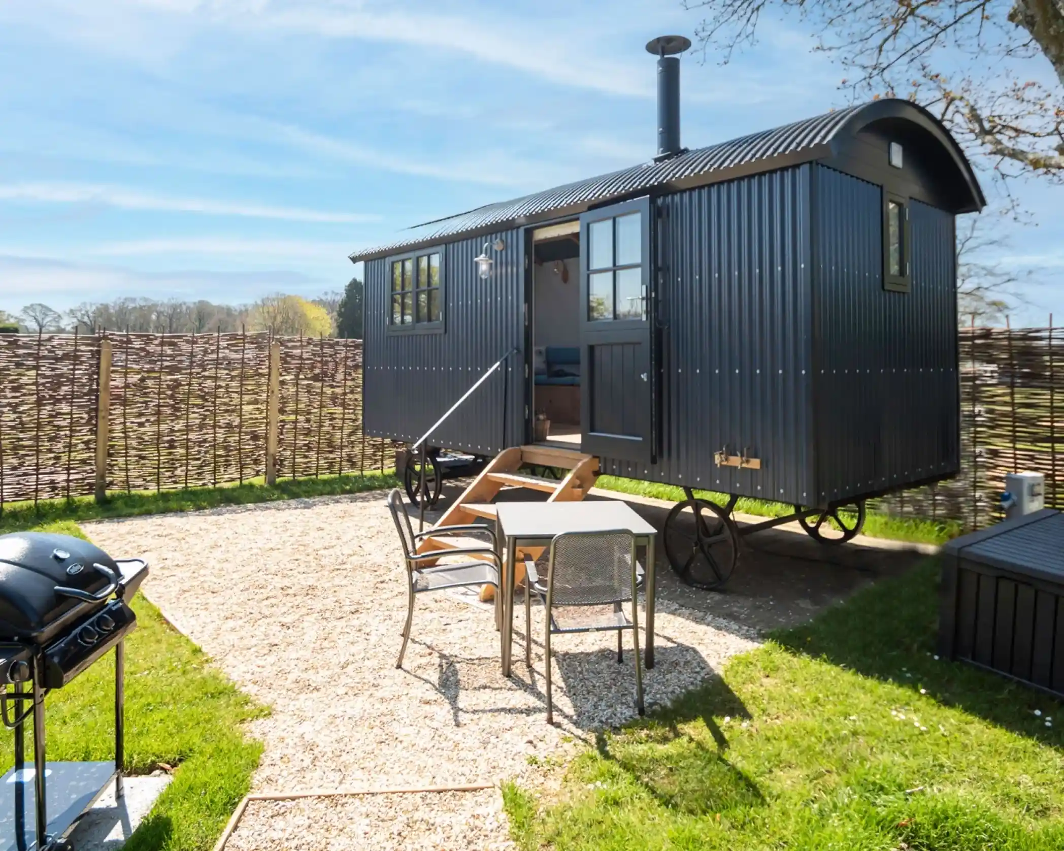 Modern black shepherd’s hut with outdoor seating area and barbecue in a private garden.