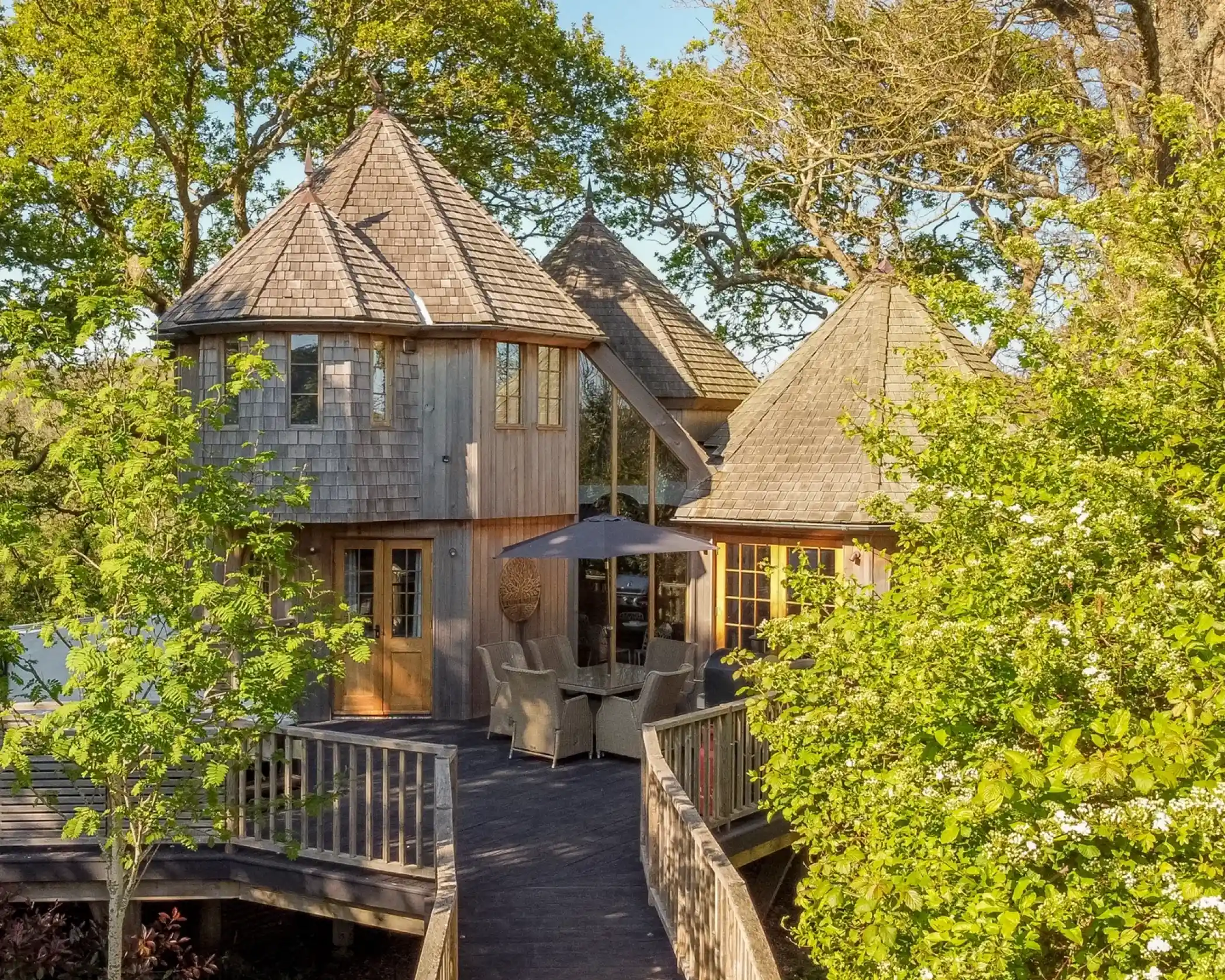 Luxury wooden treehouse with turrets and outdoor terrace surrounded by green woodland.
