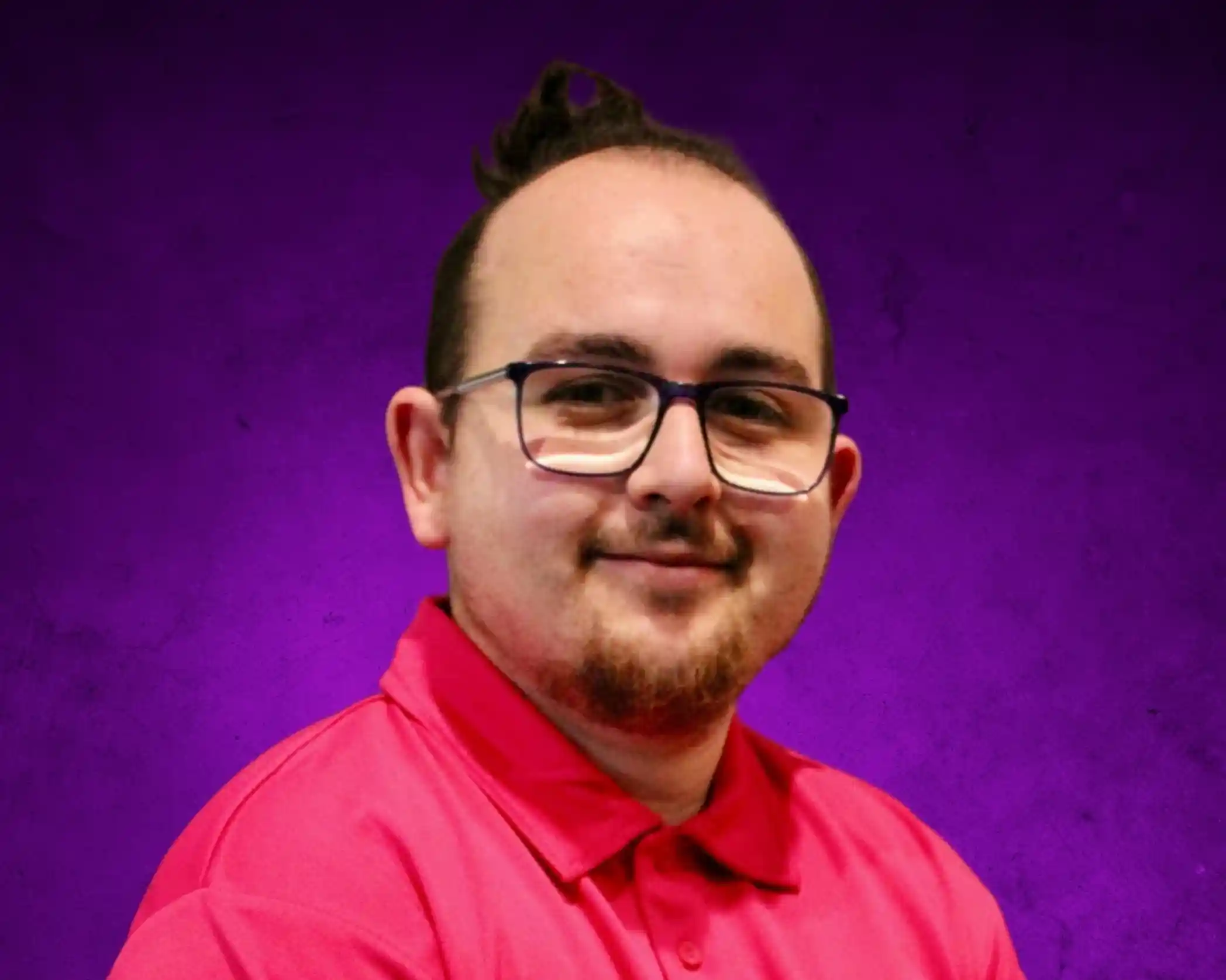 A smiling person with short, styled hair and glasses wears a bright pink shirt. The background is a textured purple.