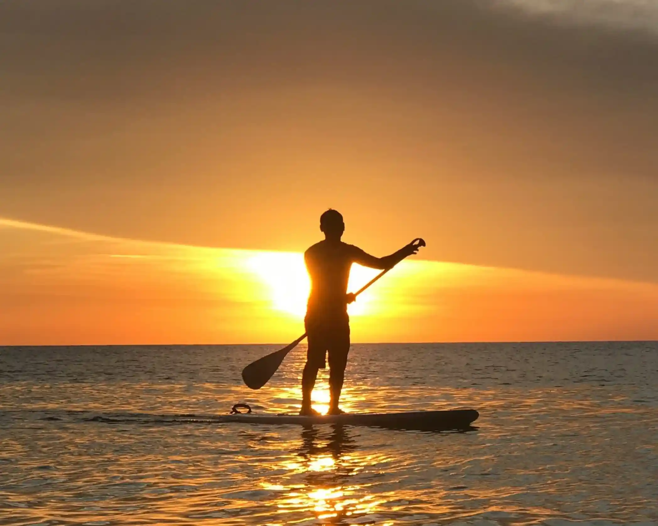 Silhouette of a person paddleboarding against a vibrant sunset over calm water.