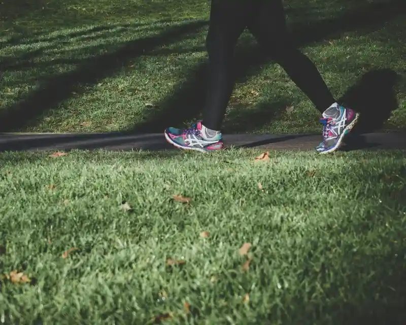 A person walks along a path on grassy ground, wearing vibrant running shoes and black leggings.