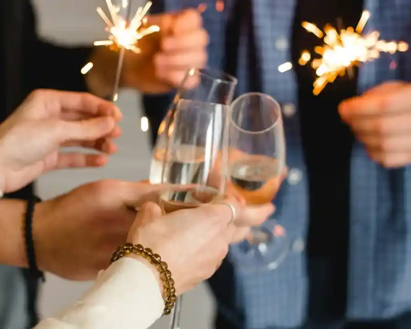 Champagne flutes clinking together, surrounded by hands holding sparklers, celebrating a special occasion.