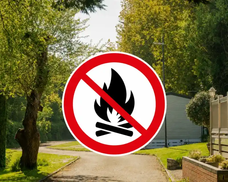 A scenic path lined with trees and a mobile home in the background features a prominent "No Fires" sign with a crossed-out flame symbol superimposed.