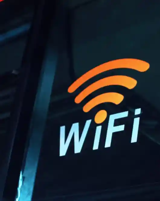 Orange WiFi symbol above the word 'WiFi' in white text, displayed on a glass window or door, indicating available wireless internet access.