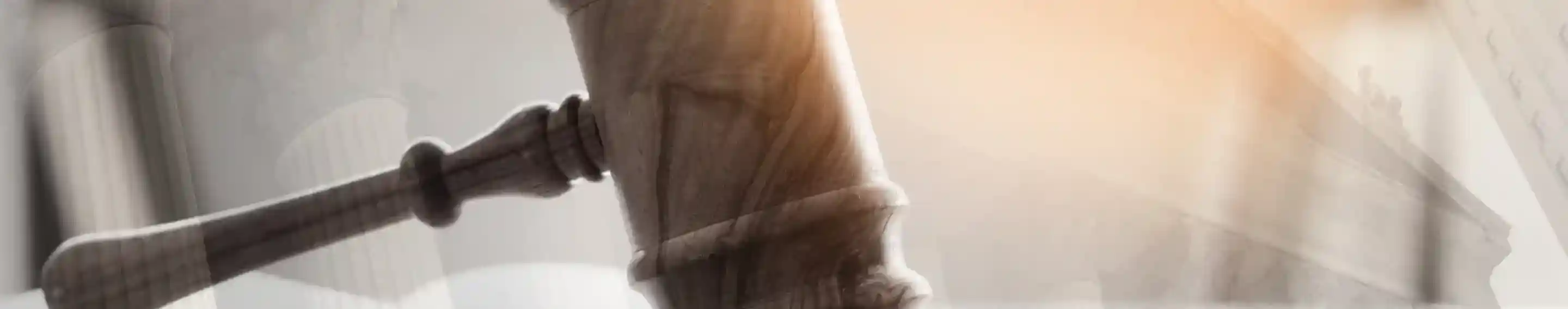 A wooden gavel rests on an open law book, symbolizing justice and legal proceedings. Soft light and abstract architectural elements blur in the background.