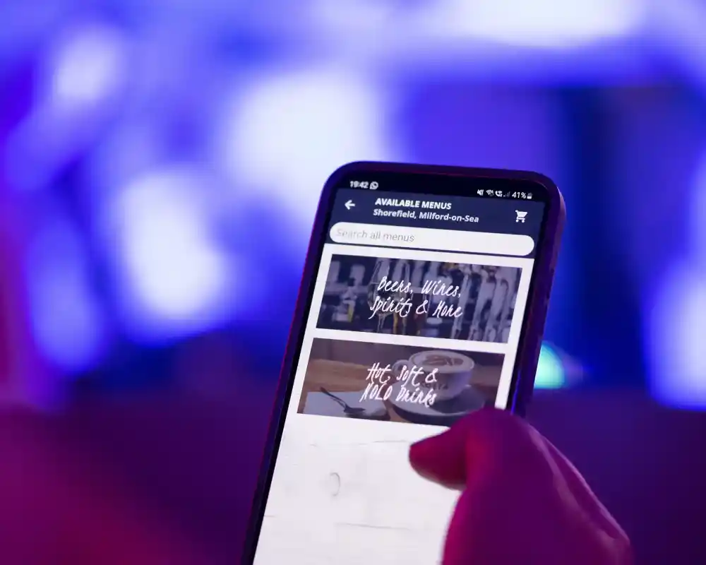 A hand holding a smartphone displaying a digital menu on a screen with colorful lighting in the background.
