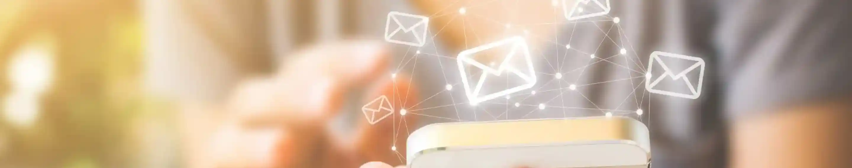 A person holding a smartphone with floating email icons above it, symbolizing communication and digital messaging. Soft lighting creates a warm ambiance in the background.