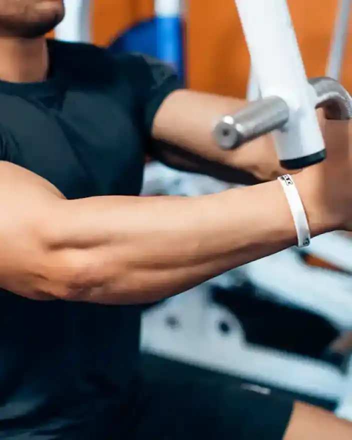 A person with muscular arms is using gym equipment, gripping metal handles tightly. The background features various exercise machines, suggesting a fitness environment.