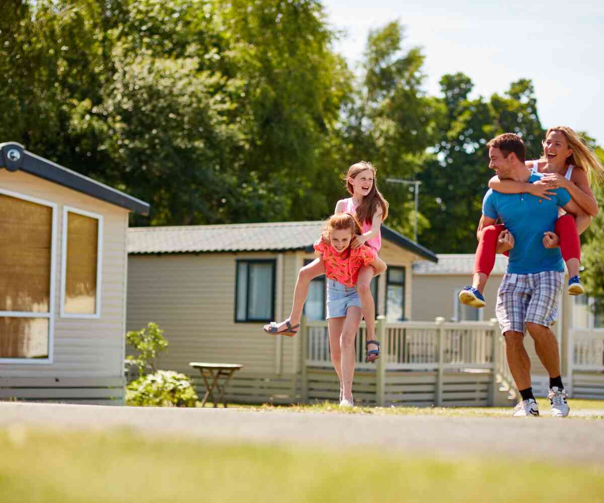 A group of animated characters from a children's show stands together, wearing colorful outfits. They are set against a backdrop of amusement park attractions, including colorful hot air balloons. The characters are smiling and appear cheerful.