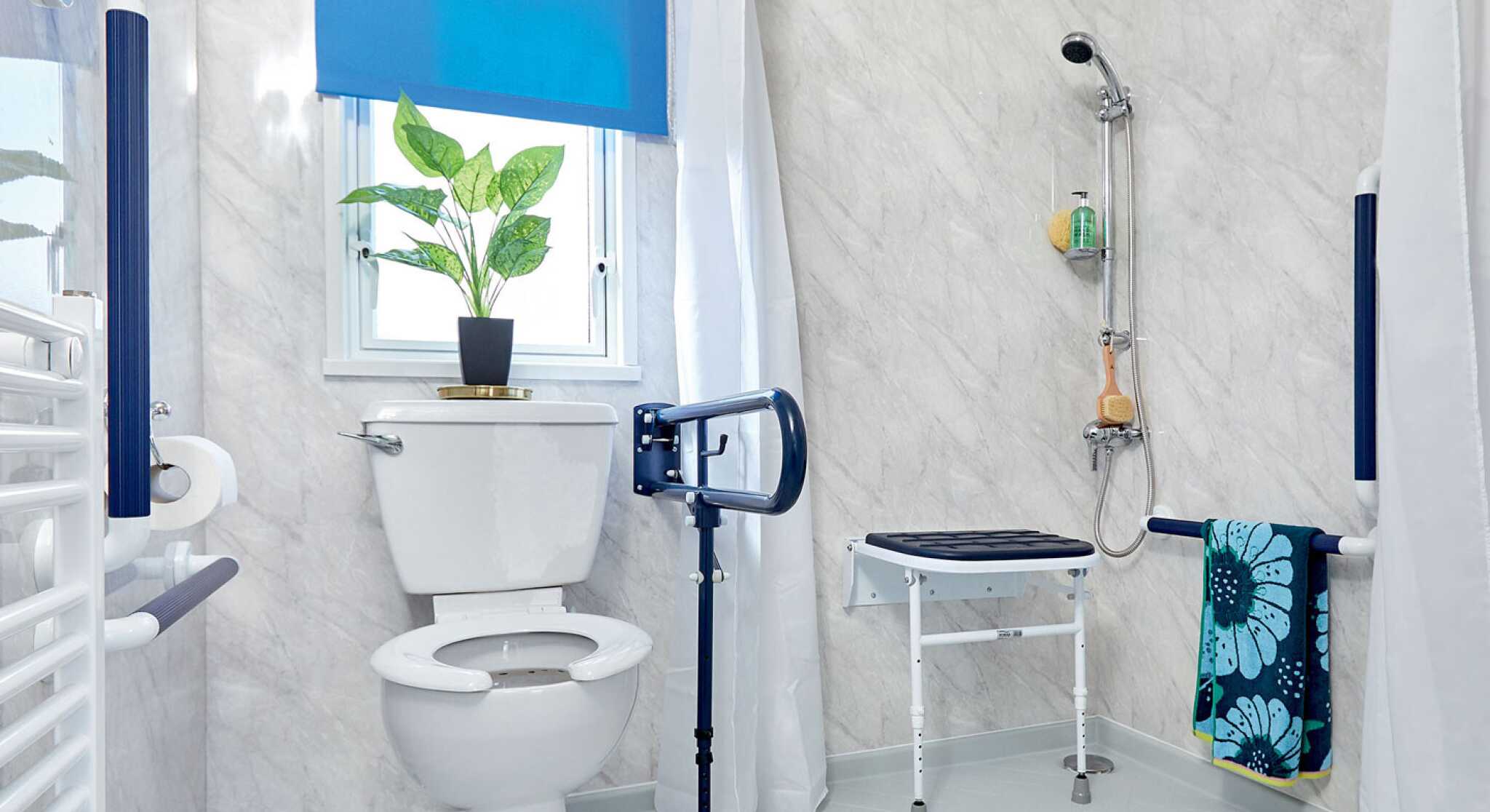 A bright and modern bathroom featuring a white toilet, grab bars, a shower with a handheld fixture, and a shower bench. A blue roller blind covers the window, and a potted plant sits on the windowsill. A towel hangs from a rack, adding a pop of color.