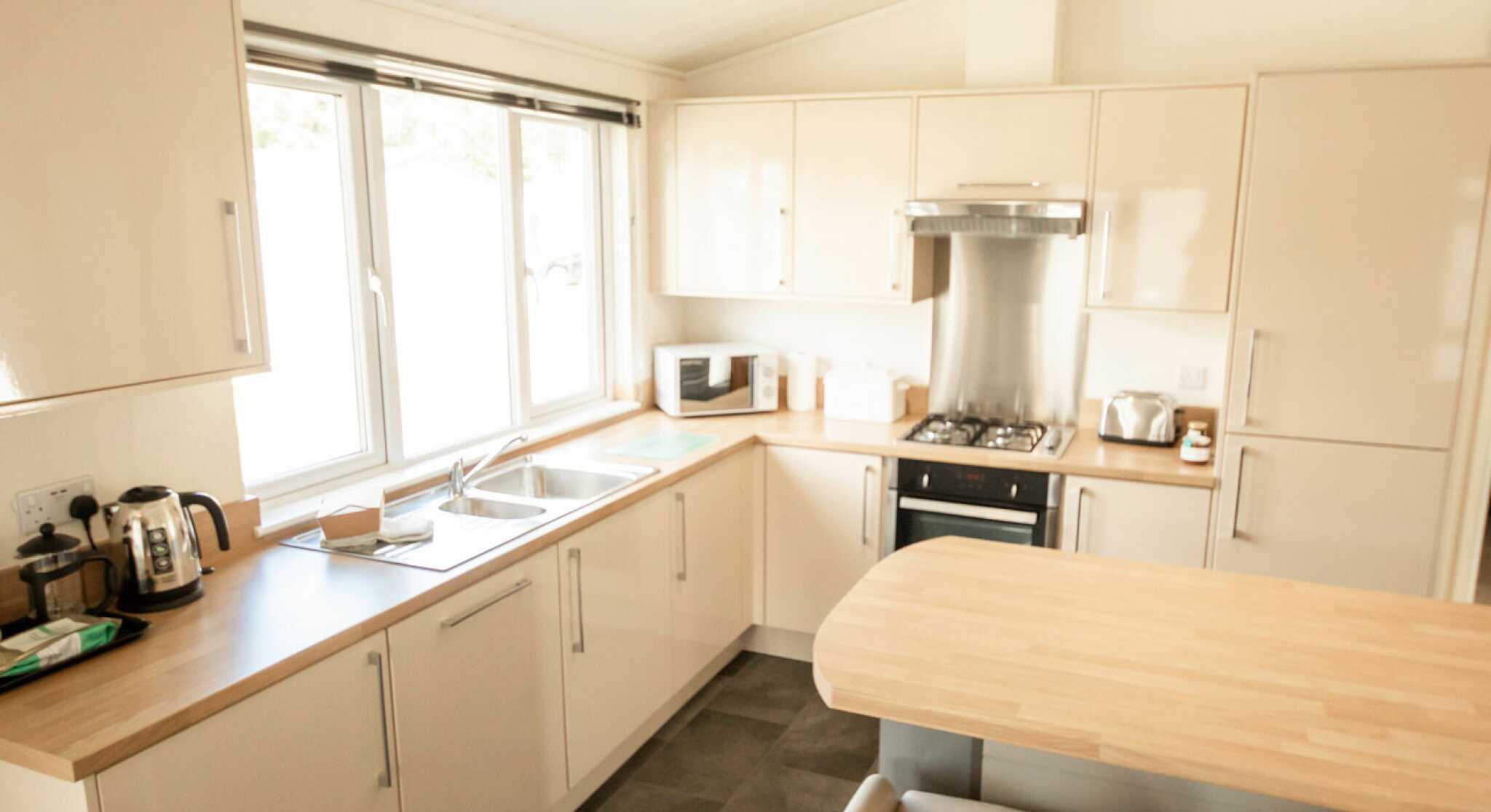 Bright, modern kitchen featuring light-colored cabinetry, a wooden countertop, and stainless steel appliances. A window allows natural light to fill the space, and a small table with two white chairs adds to the inviting atmosphere.