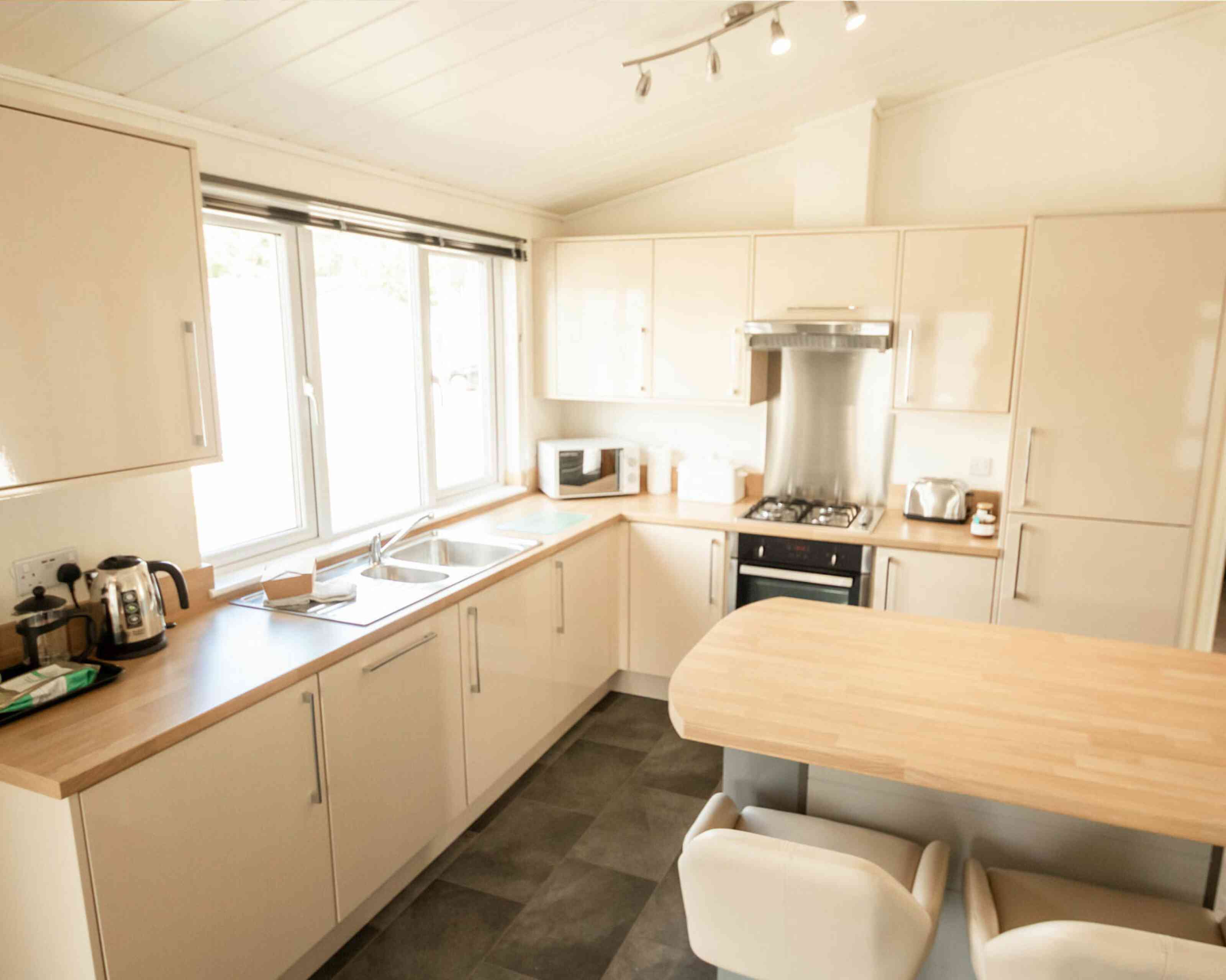 Bright, modern kitchen featuring light-colored cabinetry, a wooden countertop, and stainless steel appliances. A window allows natural light to fill the space, and a small table with two white chairs adds to the inviting atmosphere.