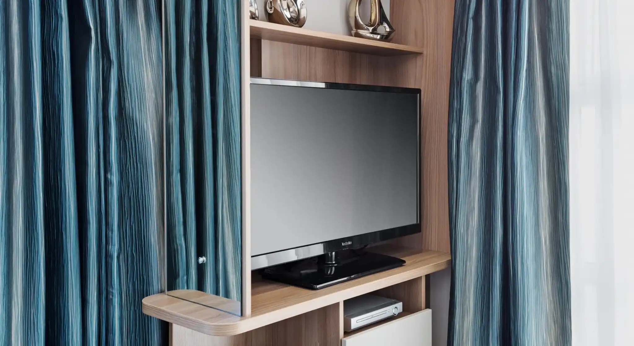 A sleek wooden entertainment unit featuring a flat-screen television, blue decorative vases, and stylish ornaments. The unit is flanked by luxurious, flowing blue curtains.