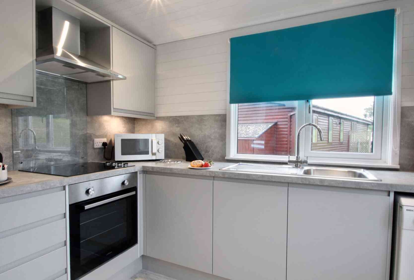Modern kitchen featuring gray cabinets, stainless steel appliances, and a turquoise blind over the window. A countertop with a sink and microwave is visible, along with a few utensils and a plate of food.