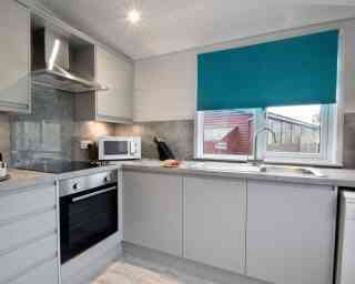 Modern kitchen featuring gray cabinets, stainless steel appliances, and a turquoise blind over the window. A countertop with a sink and microwave is visible, along with a few utensils and a plate of food.