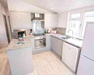 A modern kitchen featuring light gray cabinets, a stainless steel oven, and a white dishwasher. The countertop is a light gray stone, and there is a window above the sink providing natural light. Appliances include a microwave and a kettle, with a small decorative tray on the counter.