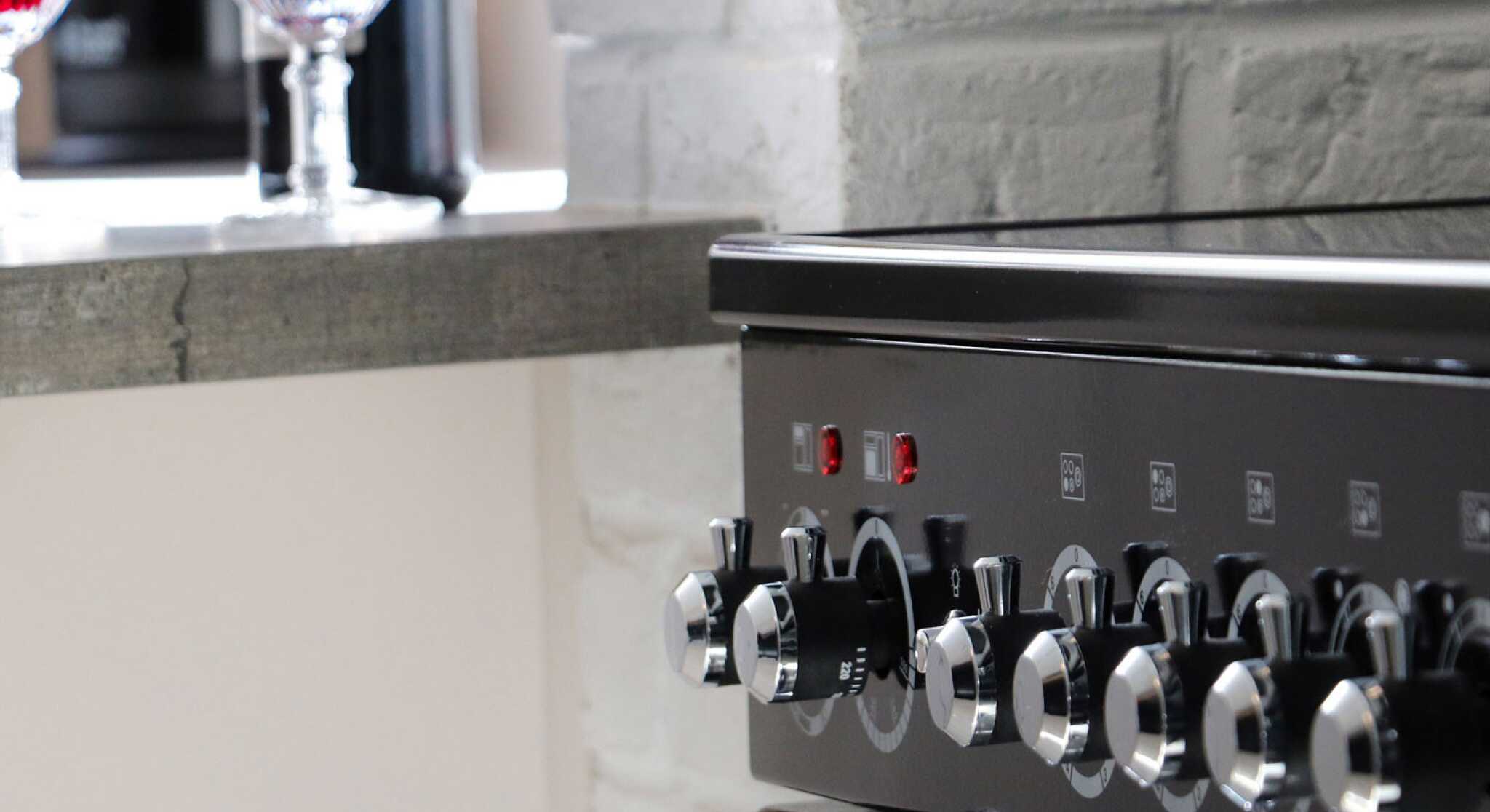 A close-up of a black oven with shiny knobs, alongside a countertop featuring two glasses of red wine.