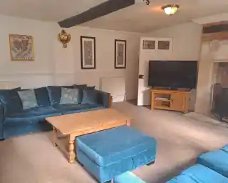 A cozy living room featuring a blue plush sofa set with decorative cushions, a wooden coffee table, and a flat-screen TV on a wooden stand. The walls are adorned with framed artwork, and a fireplace is visible in the corner.