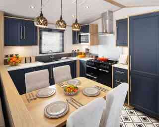 A modern kitchen featuring navy blue cabinetry, a wooden countertop, and a dining area with a table set for four. Pendant lights hang above the table, and a black stove is visible in the background. Fresh salad is placed in the center of the table against a patterned floor.