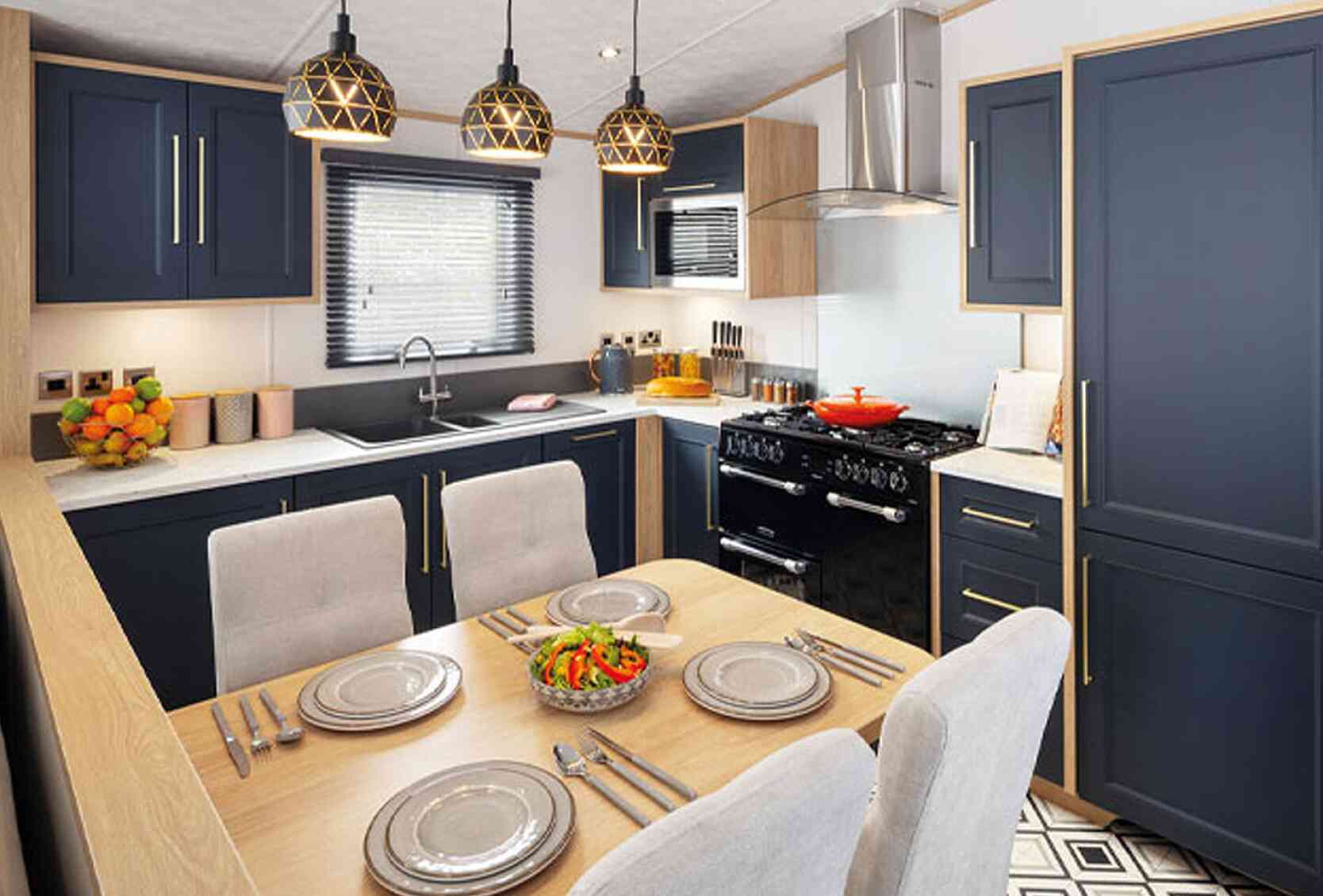 A modern kitchen featuring navy blue cabinetry, a wooden countertop, and a dining area with a table set for four. Pendant lights hang above the table, and a black stove is visible in the background. Fresh salad is placed in the center of the table against a patterned floor.
