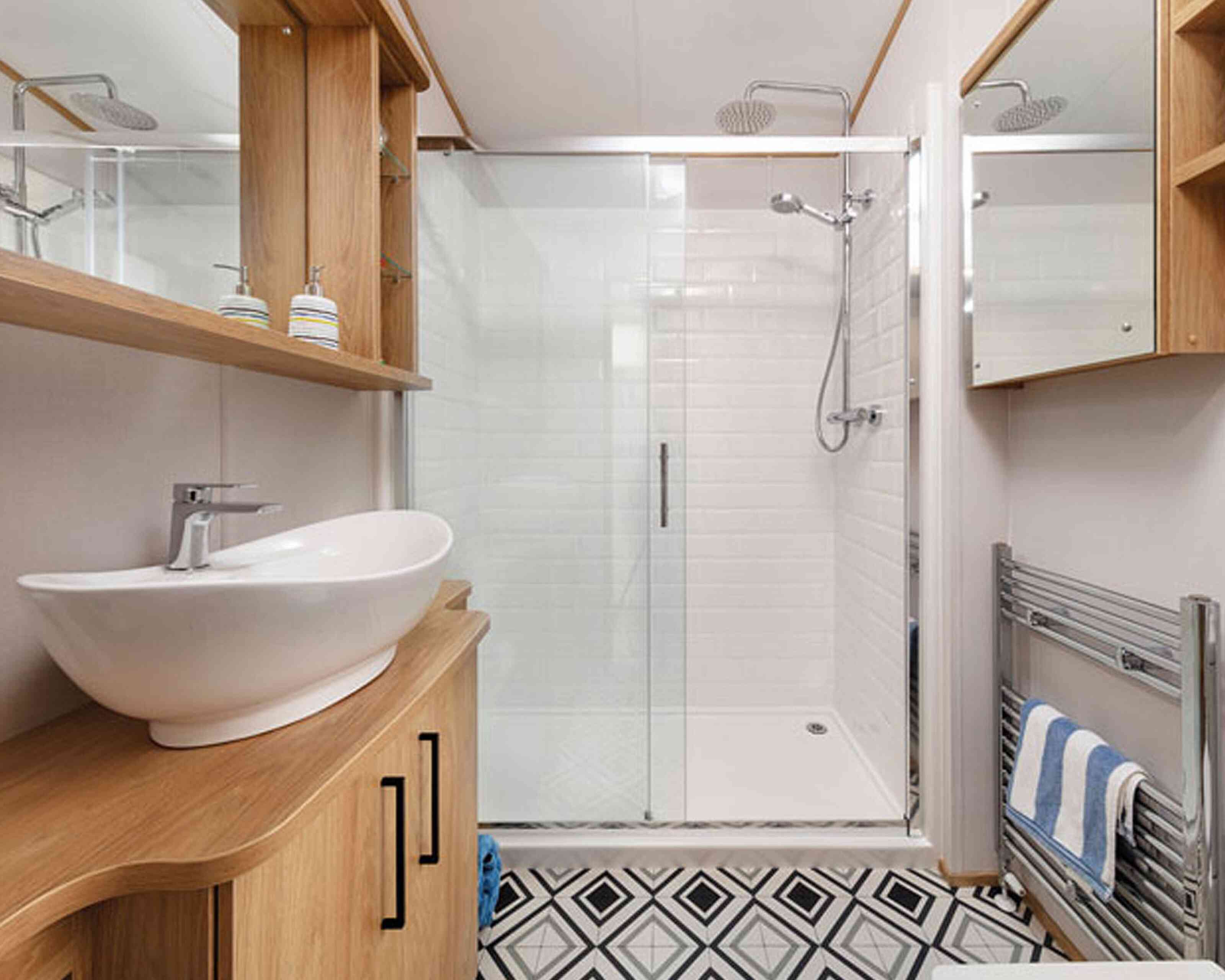 Modern bathroom featuring a walk-in shower with glass doors, a sleek white basin on a wooden vanity, and a stylish patterned floor. Wood shelves display toiletries, and a heated towel rack adds convenience.