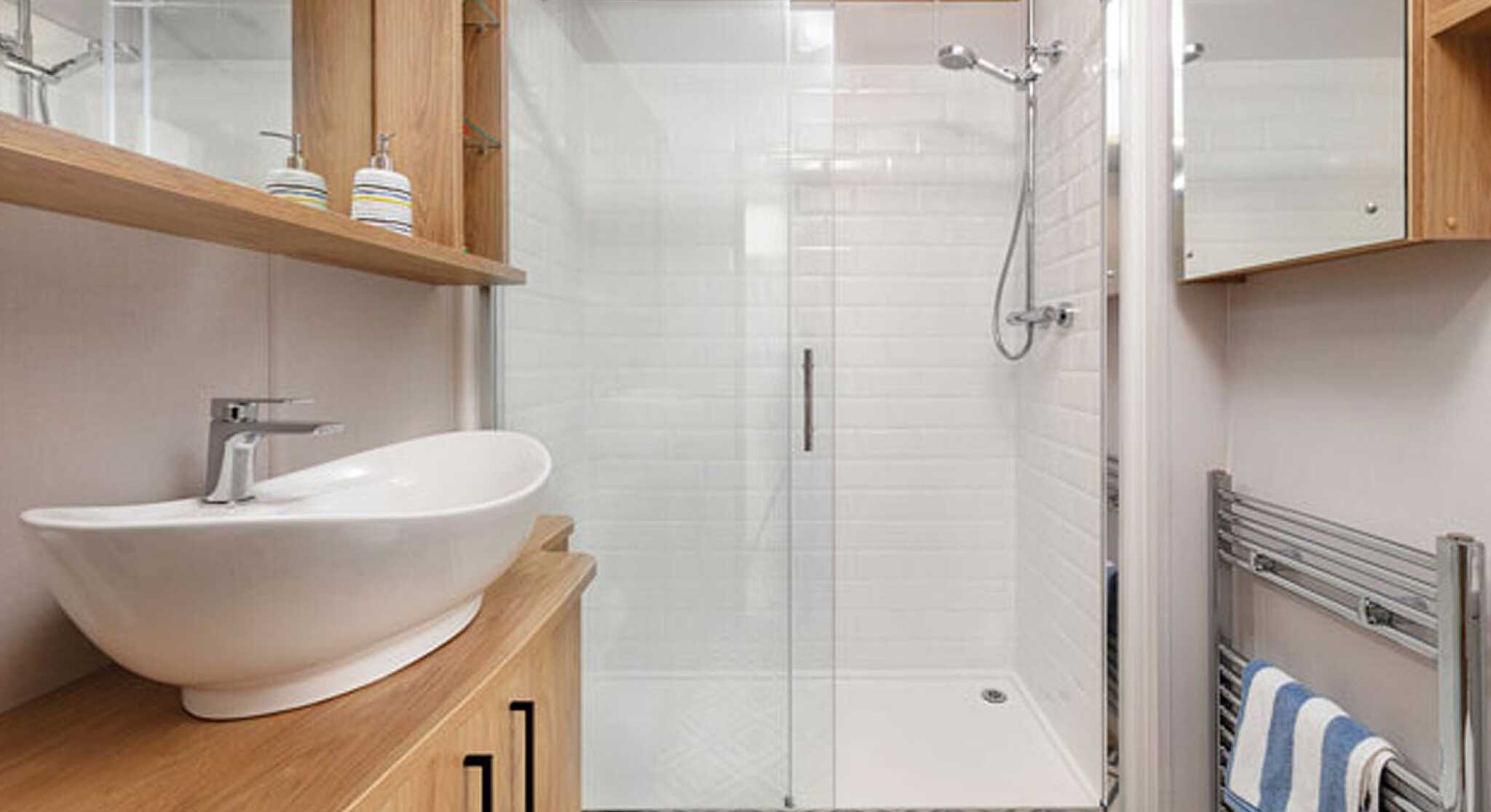 Modern bathroom featuring a walk-in shower with glass doors, a sleek white basin on a wooden vanity, and a stylish patterned floor. Wood shelves display toiletries, and a heated towel rack adds convenience.