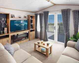 A cozy living room featuring a light-colored sofa, a modern entertainment unit with a television displaying a marine scene, and a coffee table with snacks. Large curtains frame the window that leads to a balcony, with a view of greenery outside. Soft lighting adds warmth to the space.