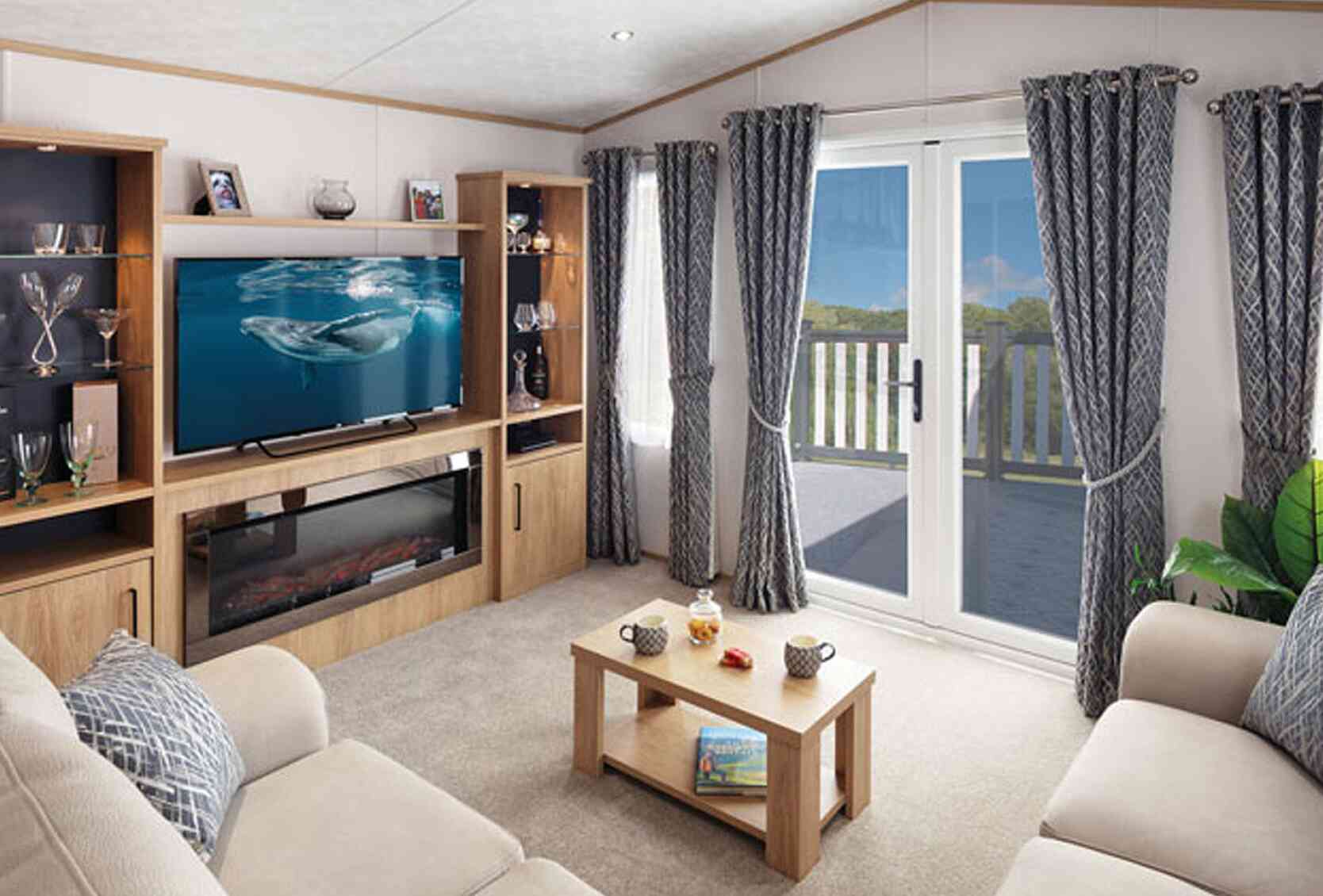 A cozy living room featuring a light-colored sofa, a modern entertainment unit with a television displaying a marine scene, and a coffee table with snacks. Large curtains frame the window that leads to a balcony, with a view of greenery outside. Soft lighting adds warmth to the space.