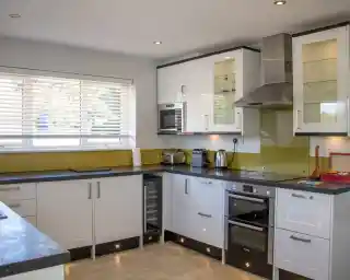 Modern kitchen featuring white and black cabinetry, a stainless steel oven, a built-in microwave, and a wine cooler. There are countertop appliances like a toaster and kettle, with natural light streaming through a window with blinds. A sleek design and clean lines are emphasized throughout the space.