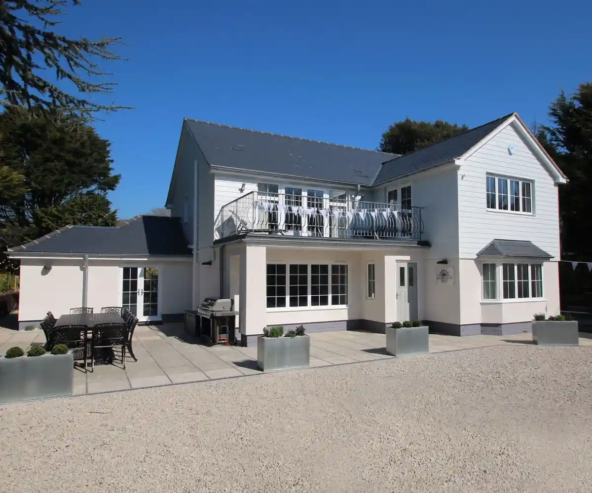A row of static caravans is set in a lush green area, with a circular flower bed filled with vibrant blooms in the foreground. Tall trees and a clear blue sky complete the tranquil scene.