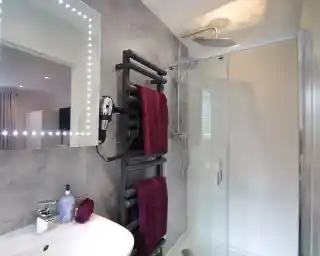 Modern bathroom featuring a glass shower enclosure, a sleek towel warmer with burgundy towels, a stylish sink with a mirror framed by lights, and a contemporary showerhead.