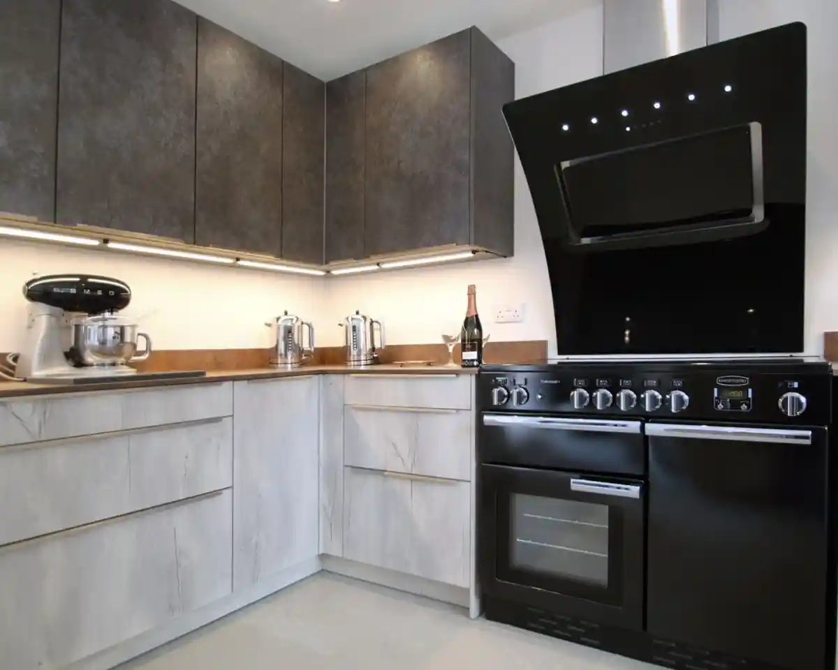Modern kitchen featuring sleek black and gray cabinetry, a black range cooker, and a mixer on the countertop. Elegant lighting highlights the workspace.