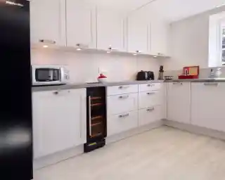 Modern kitchen featuring white cabinetry, a grey countertop, and stainless steel appliances including a microwave and a wine cooler. Bright and clean design with good lighting.