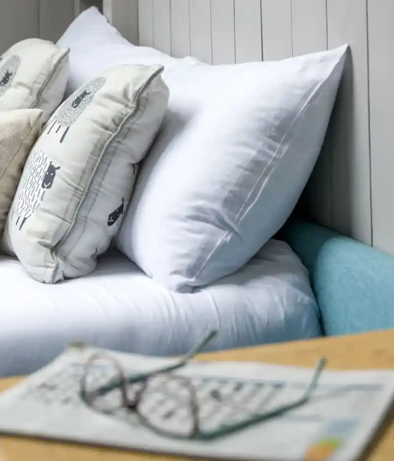 A woman and a man relax on a couch, laughing and enjoying time with a smiling boy who is sitting between them. The boy holds a drink while the woman is looking at him; they are in a bright room with greenery visible outside.