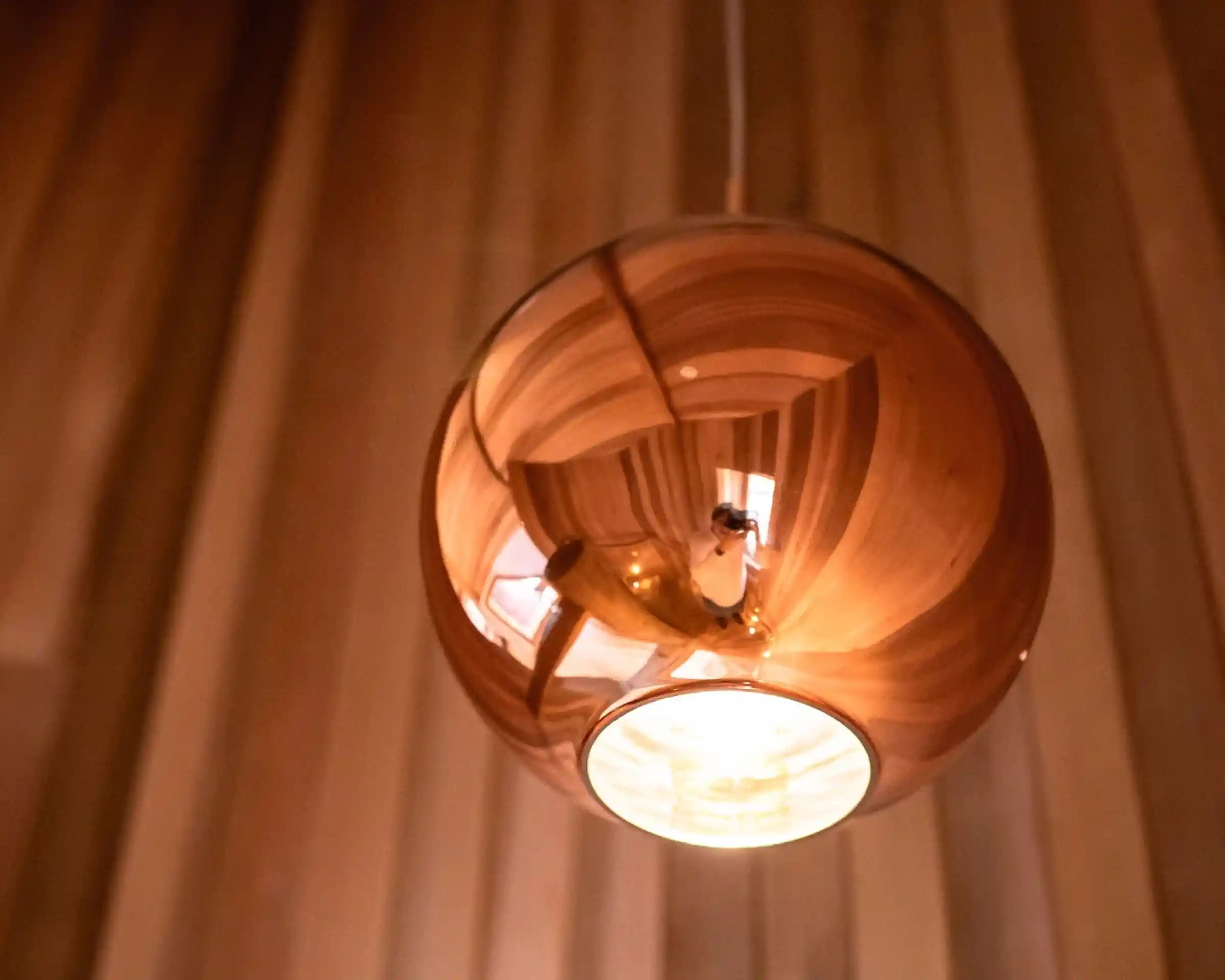 A reflective, spherical pendant light hangs from the ceiling, emanating a warm glow. The background features wooden paneling that adds a cozy ambiance.