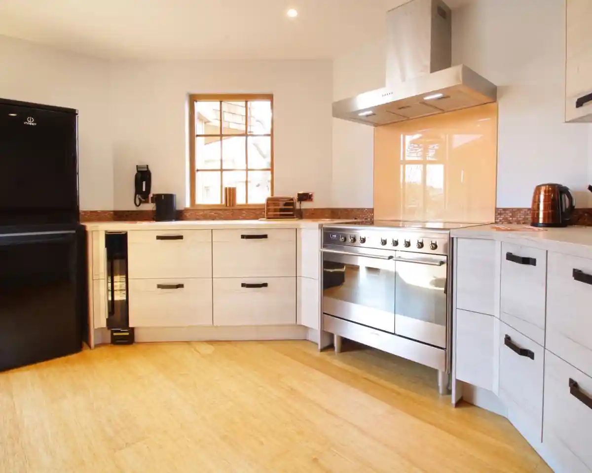 Modern kitchen featuring a sleek design with light wood cabinetry, a stainless steel range and hood, a black refrigerator, and bamboo flooring. A window allows natural light to brighten the space.
