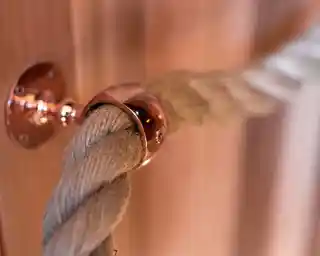 A thick natural rope secured with a shiny copper fixture attached to a wooden surface. The background has warm wood tones, creating a cozy atmosphere.