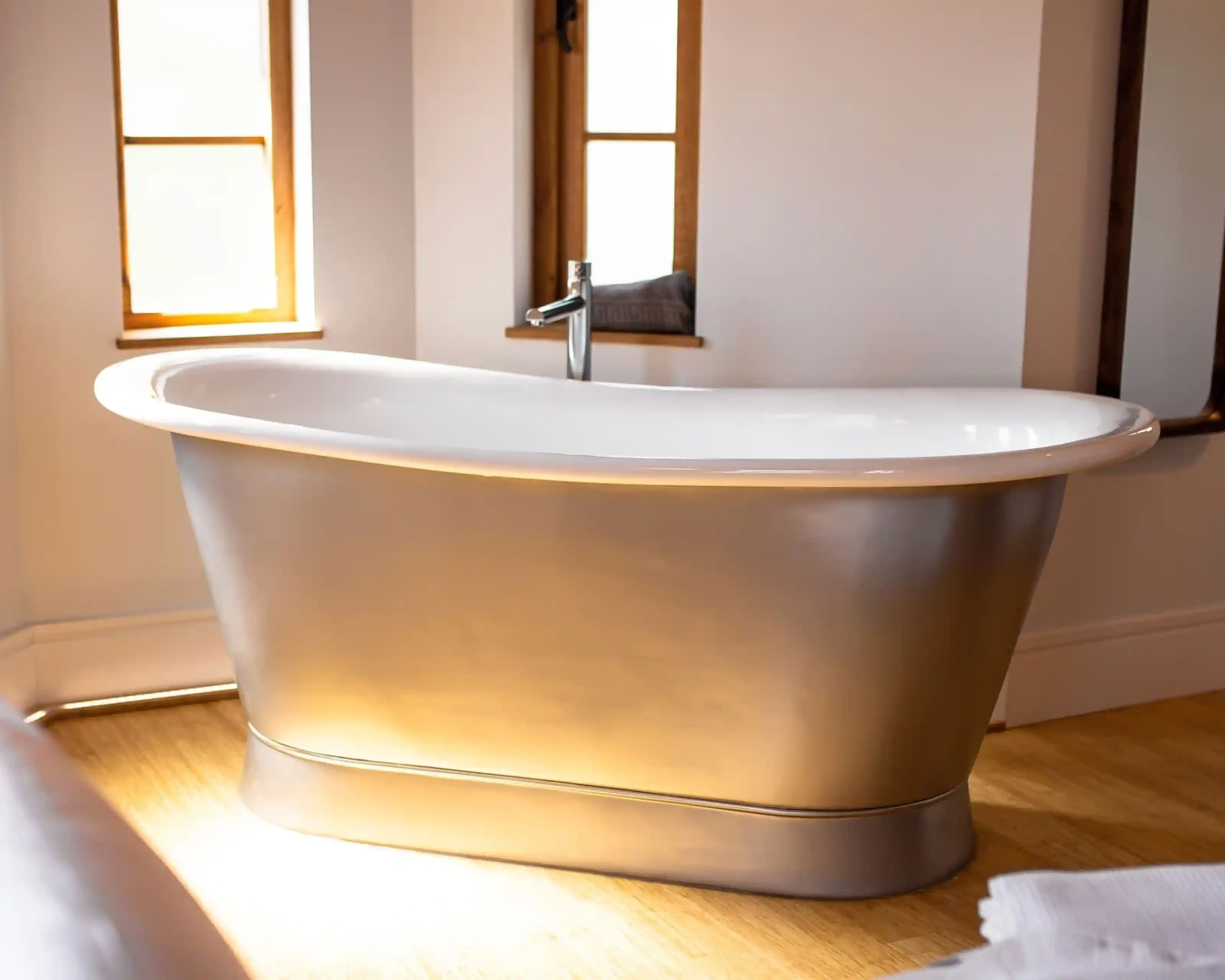 A stylish, freestanding bathtub with a sleek, curvy design, featuring a white interior and metallic gold exterior. Natural light streams in through nearby windows, accentuating the modern bathroom setting.