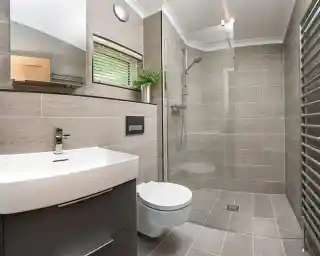Modern bathroom featuring a glass shower enclosure, a sleek white vanity with a basin, a wall-mounted toilet, and tiled walls and floors in neutral tones. A mirror and a small plant add to the contemporary design.