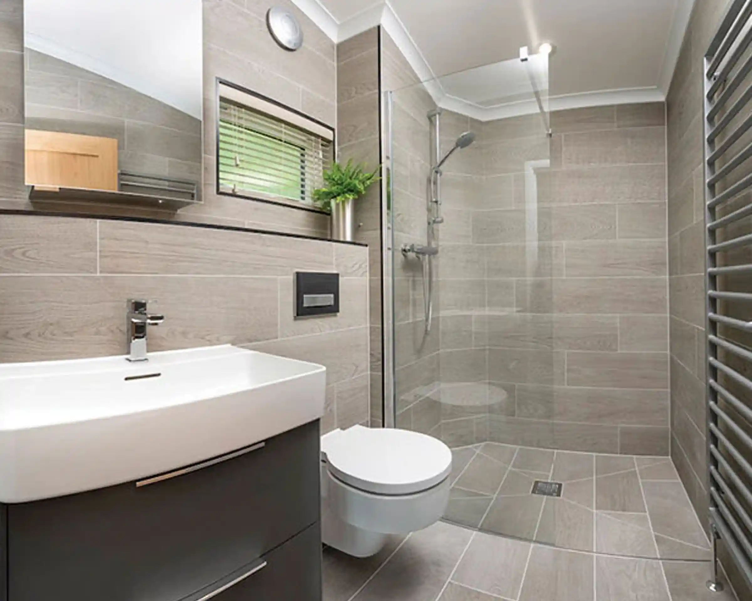 Modern bathroom featuring a glass shower enclosure, a sleek white vanity with a basin, a wall-mounted toilet, and tiled walls and floors in neutral tones. A mirror and a small plant add to the contemporary design.