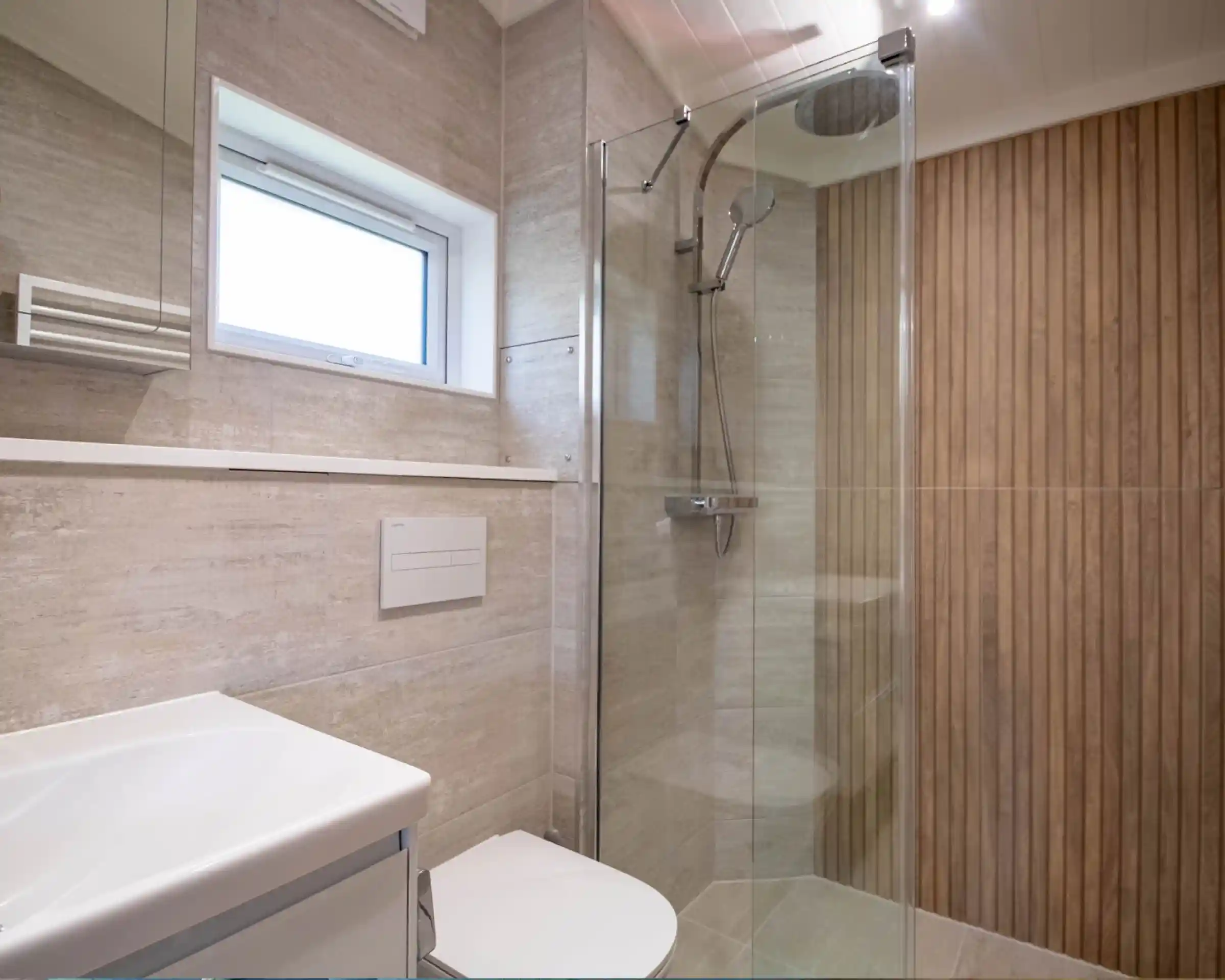 Modern bathroom featuring a glass shower stall, wooden accent wall, and a sleek sink with storage underneath. Natural light streams through a small window.