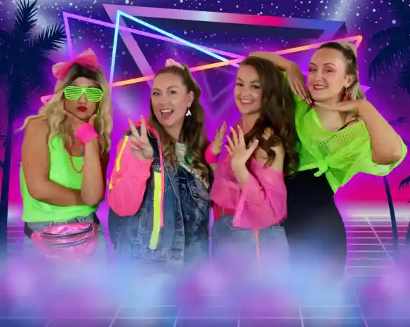 Four women pose together in colorful 1980s-inspired outfits against a vibrant, neon background featuring geometric shapes and palm trees. They display playful expressions and gestures, showcasing their bright accessories and hairstyles.