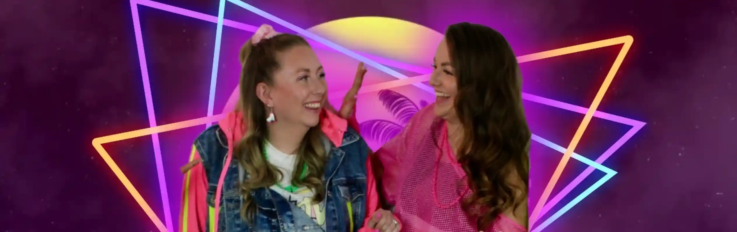 Two women in vibrant 80s-inspired outfits smile and engage playfully against a colorful, retro-themed background with neon geometric shapes and a glowing horizon.