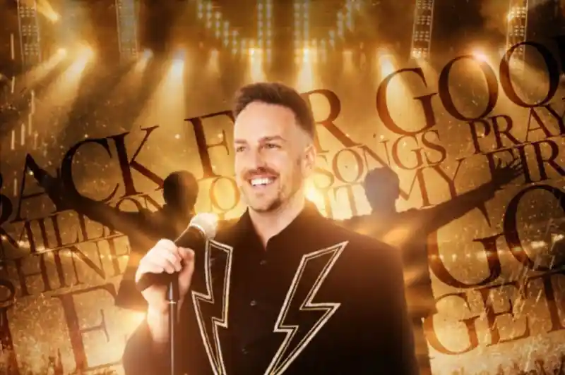 A smiling performer in a flashy jacket stands with a microphone on stage, illuminated by bright lights. The background features the words "Back for Good" and "songs," creating an energetic atmosphere.