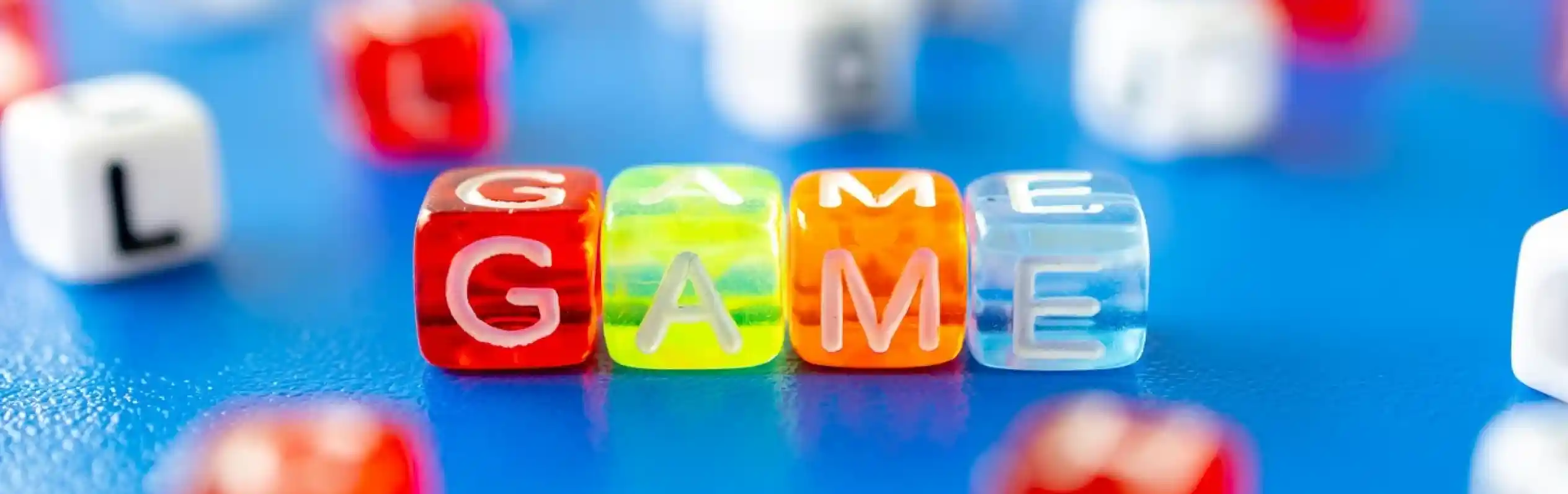 Colorful plastic letter beads spelling out "GAME," surrounded by various other letter beads on a blue surface.