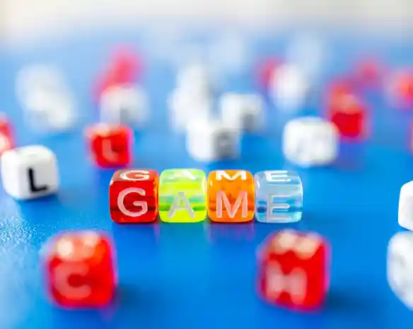 Colorful plastic letter beads spelling out "GAME," surrounded by various other letter beads on a blue surface.