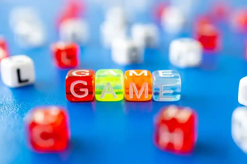 Colorful plastic letter beads spelling out "GAME," surrounded by various other letter beads on a blue surface.