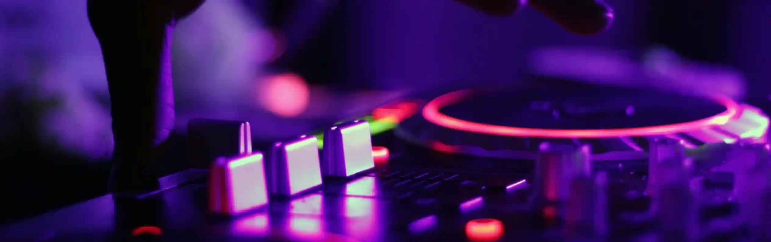 A close-up of a hand adjusting a DJ mixer with glowing knobs and buttons in purple lighting.